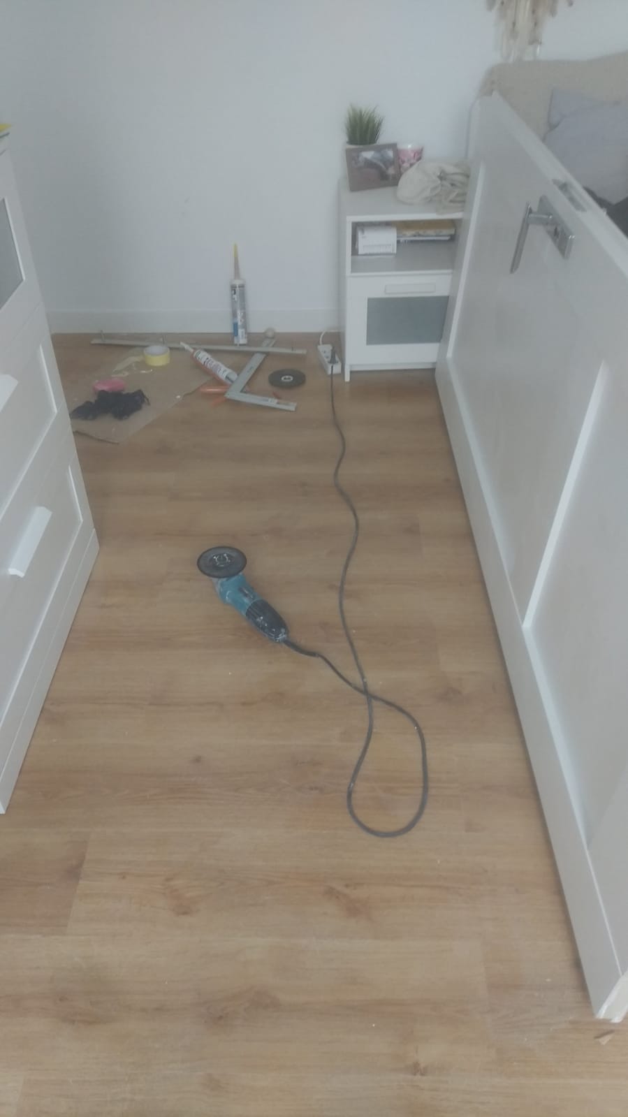 Przygotowanie do montażu listew przypodłogowych: szlifierka kątowa, kątownik, silikon i akcesoria na panelach podłogowych w trakcie wykańczania wnętrza.