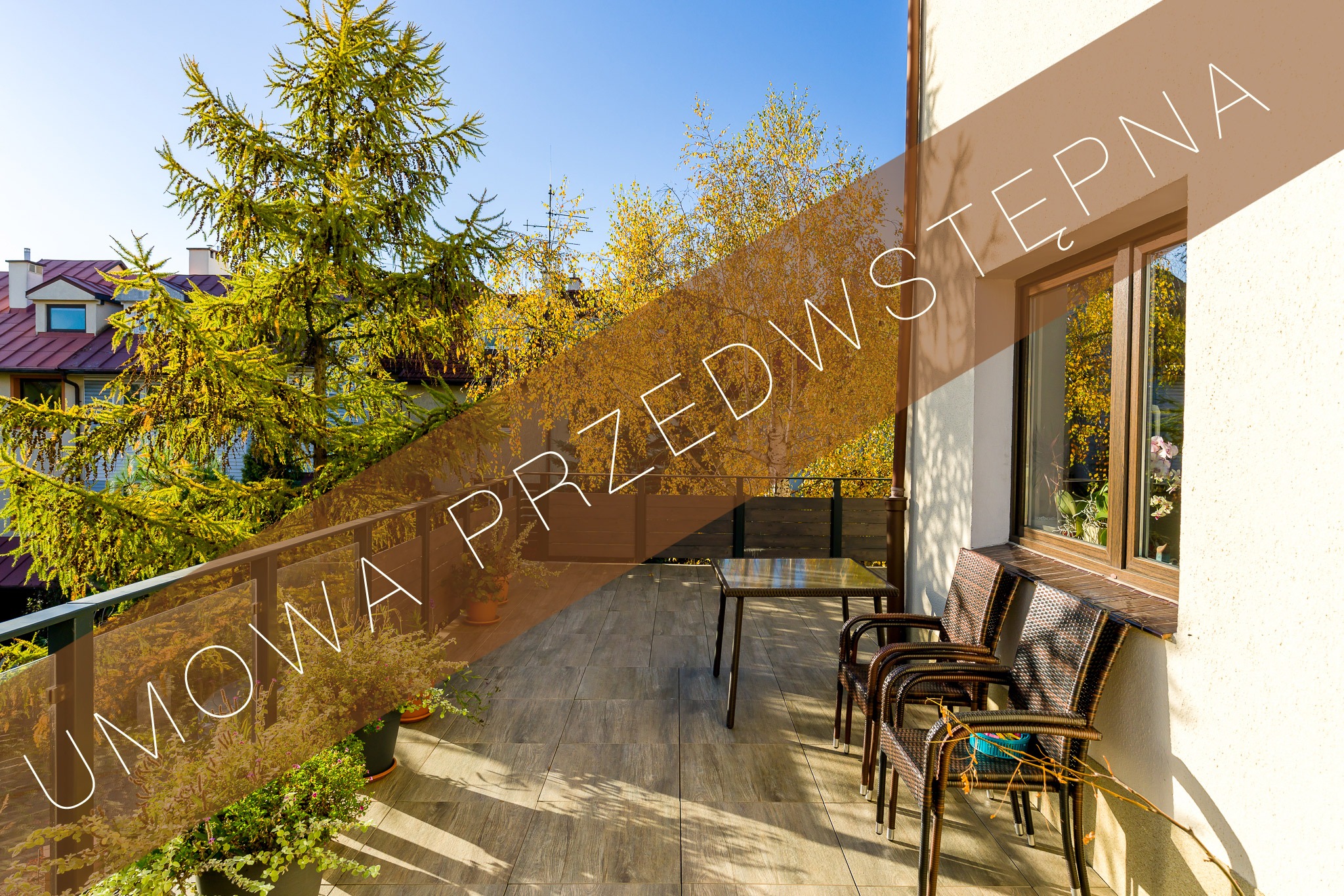 Słoneczny balkon z drewnianą podłogą i meblami rattanowymi, widok na zieleń drzew i budynki w tle, z nałożonym tekstem 'UMOWA PRZEDWSTĘPNA'.