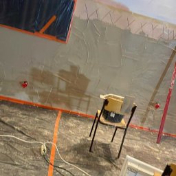 PATRYK CZEMNY - Ściana w trakcie szpachlowania, zabezpieczona folią i taśmą malarską. Widoczne narzędzia i krzesła. Prace wykończeniowe wewnątrz pomieszczenia.