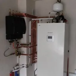 Biała pompa ciepła LG Therma V w kotłowni z widoczną instalacją miedzianą i elementami instalacji grzewczej.