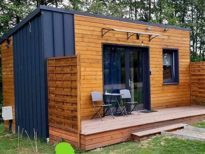 Gotowy, mały, drewniany domek z niebieskimi elementami, tarasem i dwoma krzesłami na zewnątrz.