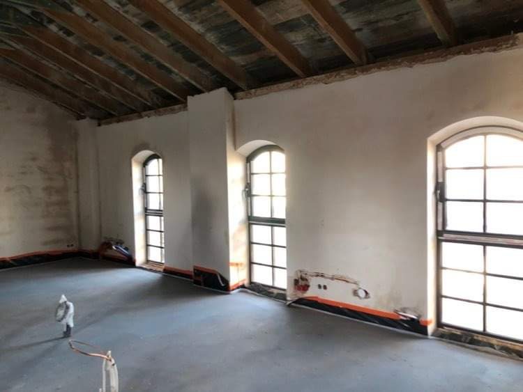 Pokój w trakcie remontu: surowe ściany z widocznymi śladami po tynkowaniu, zabezpieczona folią podłoga i okna z drewnianą stolarką, odsłonięta drewniana konstrukcja stropu.