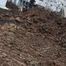 Koparka Takeuchi nabiera ziemię z pryzmy na tle nowoczesnego domu z dużymi oknami.