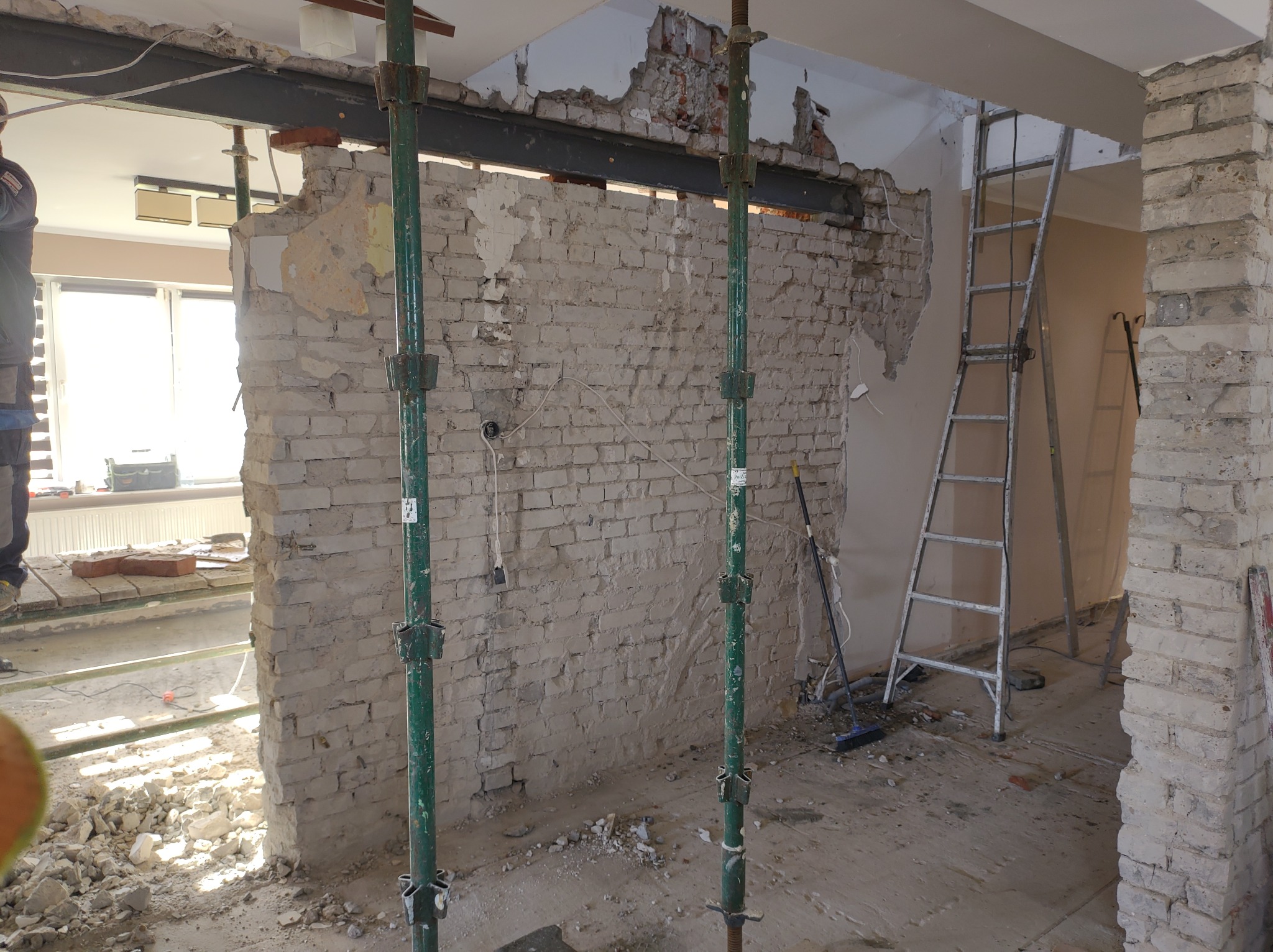 Demontaż ściany z cegły w trakcie remontu, widoczne podpory, gruz i drabina