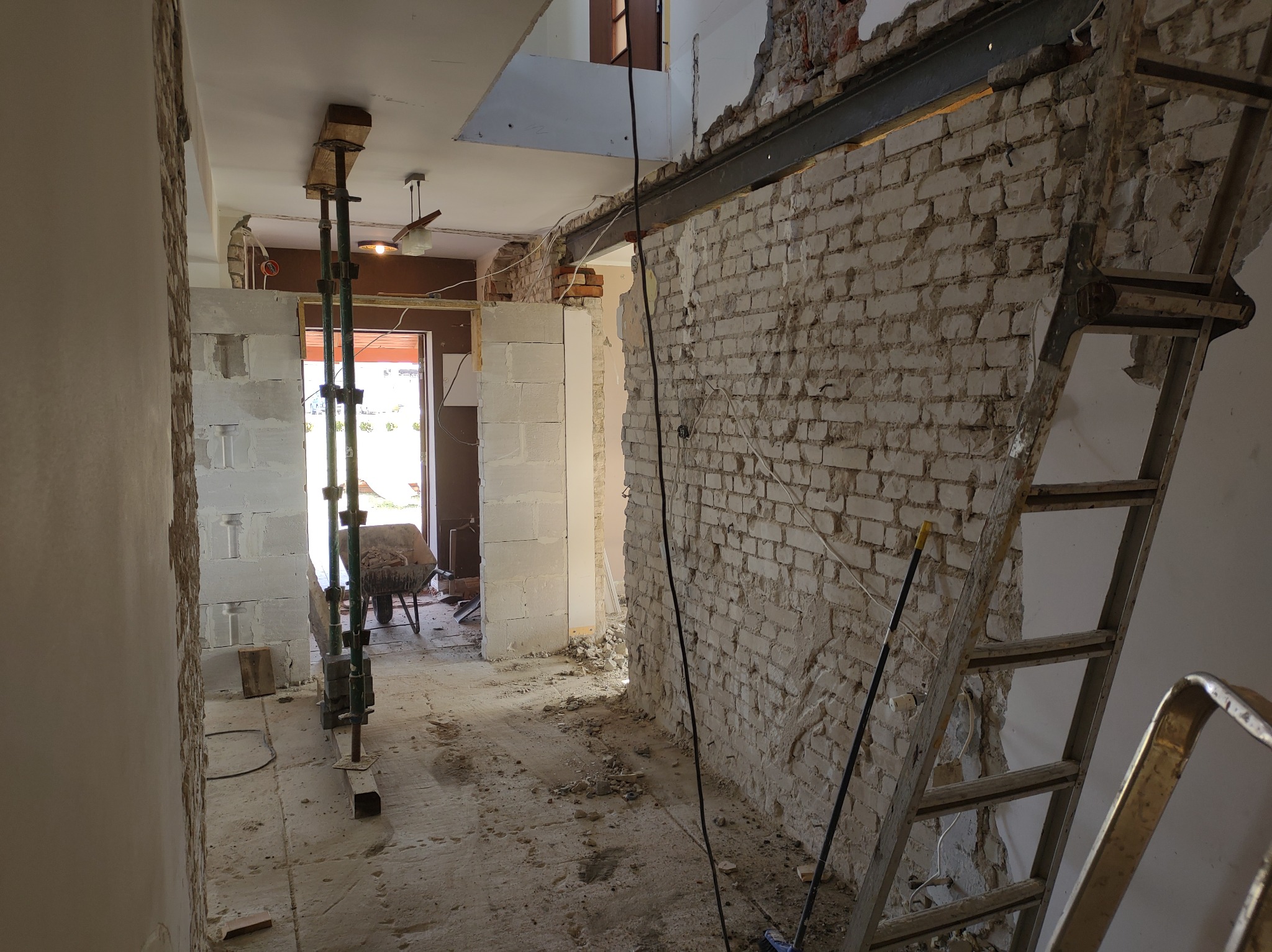 Wnętrze w trakcie prac: odsłonięta cegła, stalowa belka wzmacniająca, podpory stropu, gruz na podłodze, drabina oparta o ścianę.