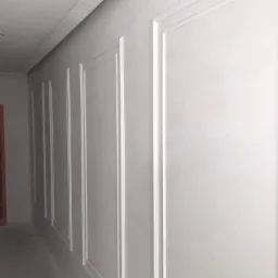 Świeżo pomalowana, jasnoszara ściana z dekoracyjnymi, białymi listwami tworzącymi prostokątne panele, widok z boku.