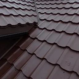 Nowy, brązowy dach z blachodachówki z kominem wentylacyjnym; dekarz w trakcie prac na połaci dachowej, widoczne łączenia i fragment rynny.