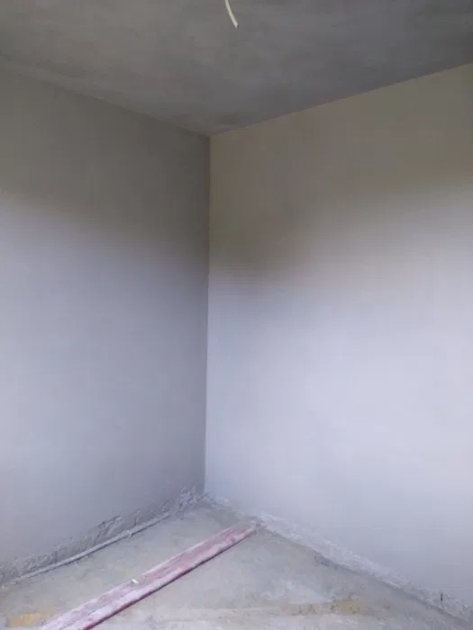 Wnętrze pokoju po nałożeniu tynków maszynowych, widoczne niedoskonałości przy podłodze i suficie, przygotowane do dalszych prac wykończeniowych.
