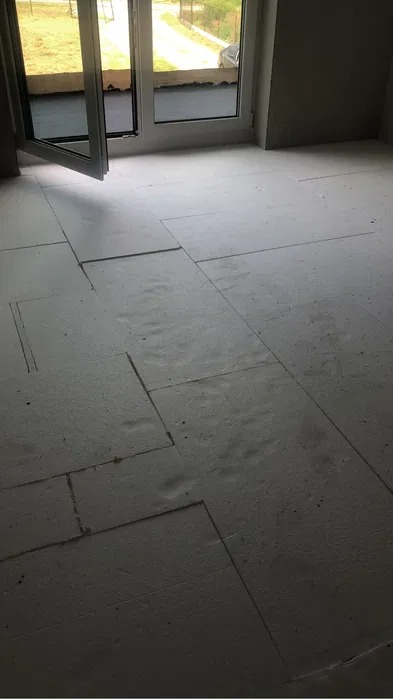 Wnętrze w stanie surowym z przygotowanym podłożem z płyt izolacyjnych na podłodze, widoczne otwarte okno balkonowe.