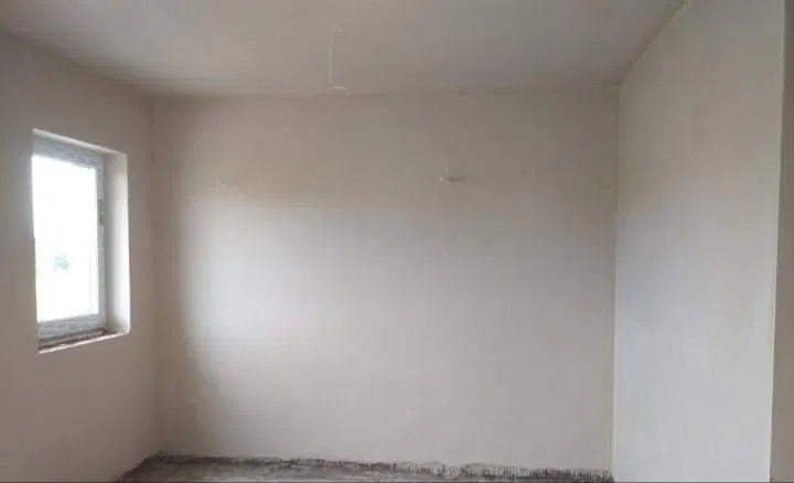 Wnętrze surowego pokoju po nałożeniu tynków maszynowych w Zagorzycach, widoczne ślady po pracach na podłodze i świeżo otynkowane ściany, okno w lewym górnym rogu.