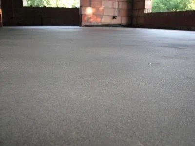 Świeżo wylana, gładka posadzka betonowa w surowym stanie, widok z niskiej perspektywy, ściany z pustaków w tle, przygotowana do dalszych prac wykończeniowych.