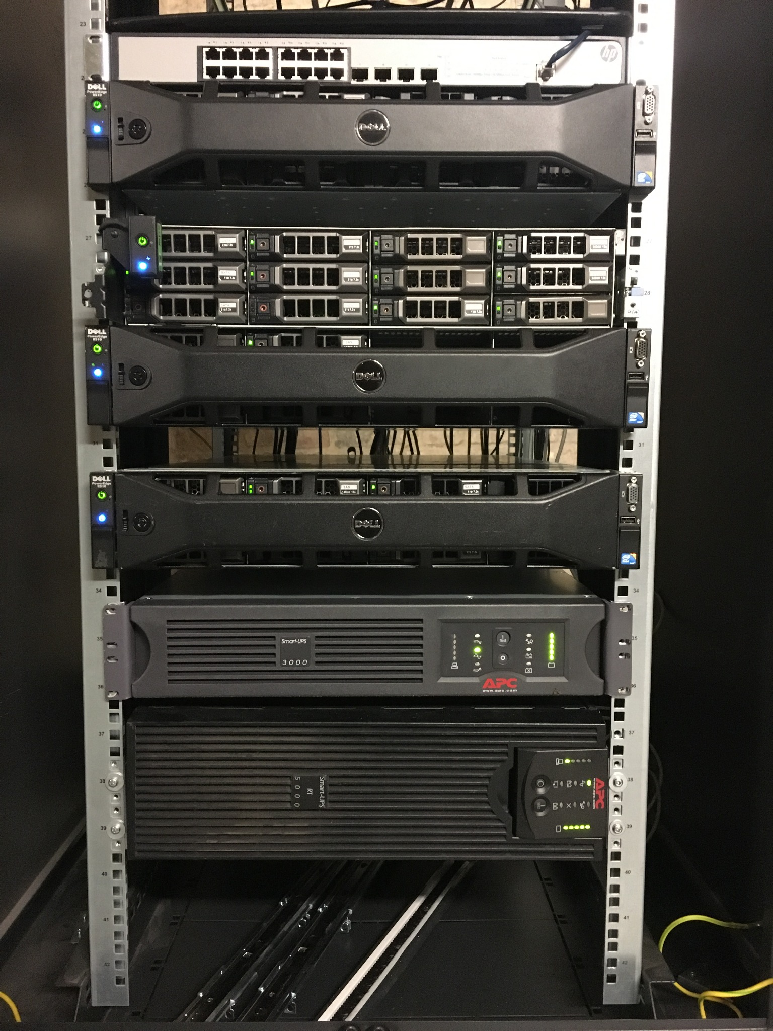 Rząd serwerów Dell PowerEdge i zasilaczy awaryjnych APC w szafie rack, widoczne diody LED stanu i etykiety urządzeń.