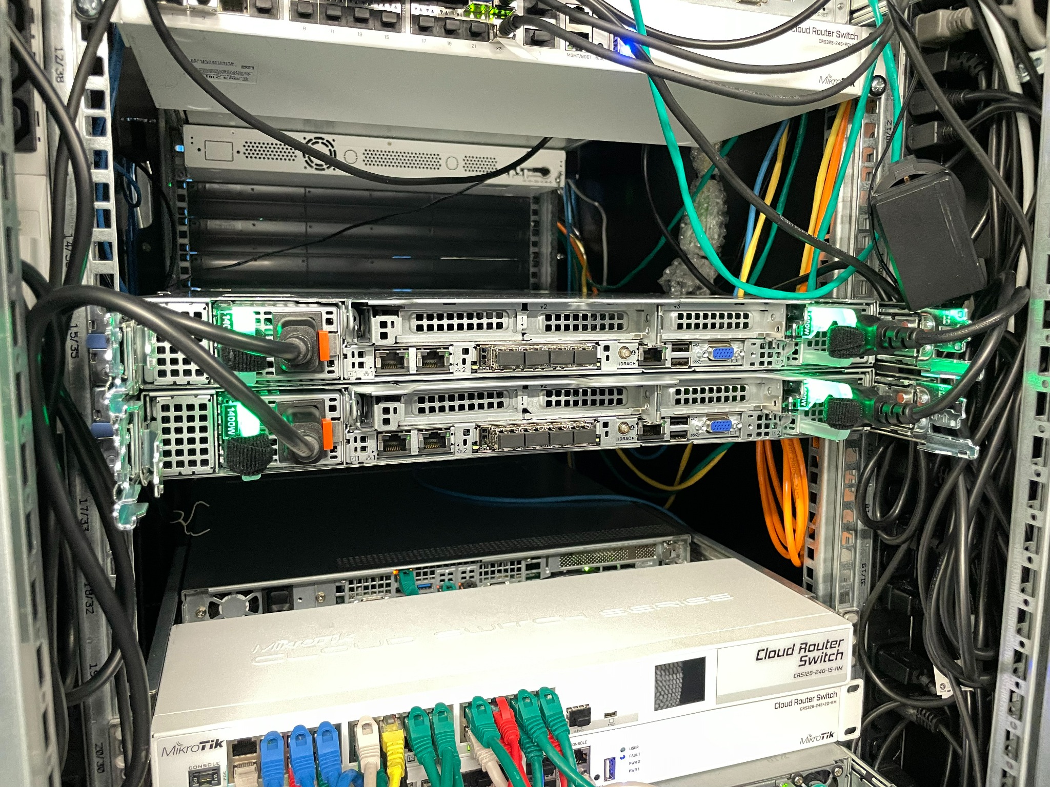 Serwery w szafie rackowej z podłączonymi kablami sieciowymi i zasilającymi, widoczne modele Cloud Router Switch firmy MikroTik.
