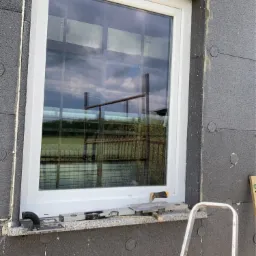 Montaż okna w ocieplonym budynku, widoczne narzędzia i drabina.