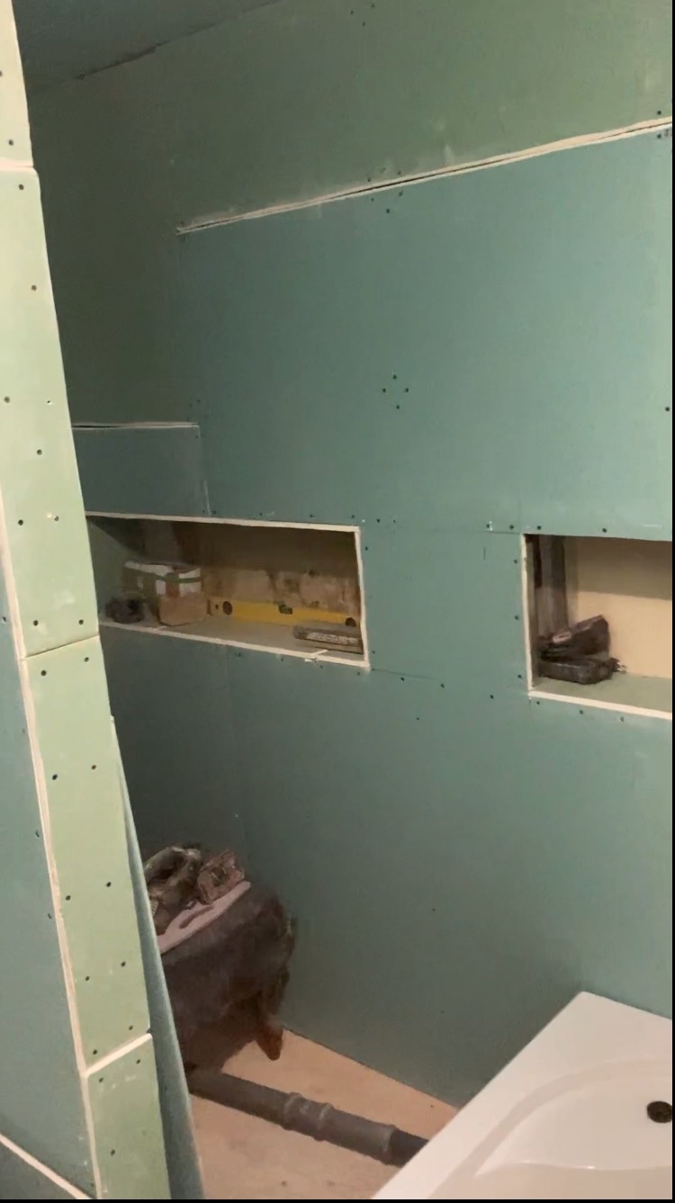 Ściana w trakcie obkładania płytami gipsowo-kartonowymi, widoczne wnęki, poziomica i fragment instalacji hydraulicznej.