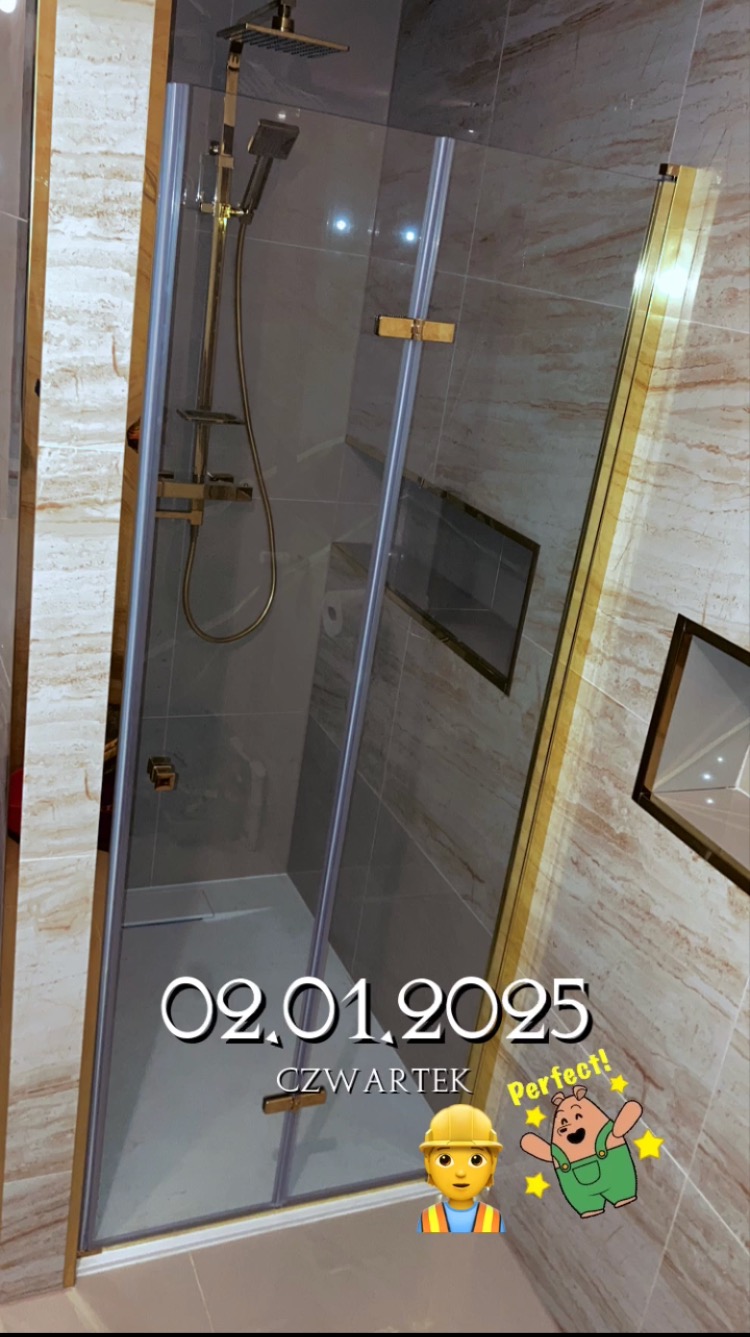 Szklana kabina prysznicowa z złotymi elementami, wbudowane półki w ścianie z marmurowym wykończeniem, widoczne naklejki cyfrowe.