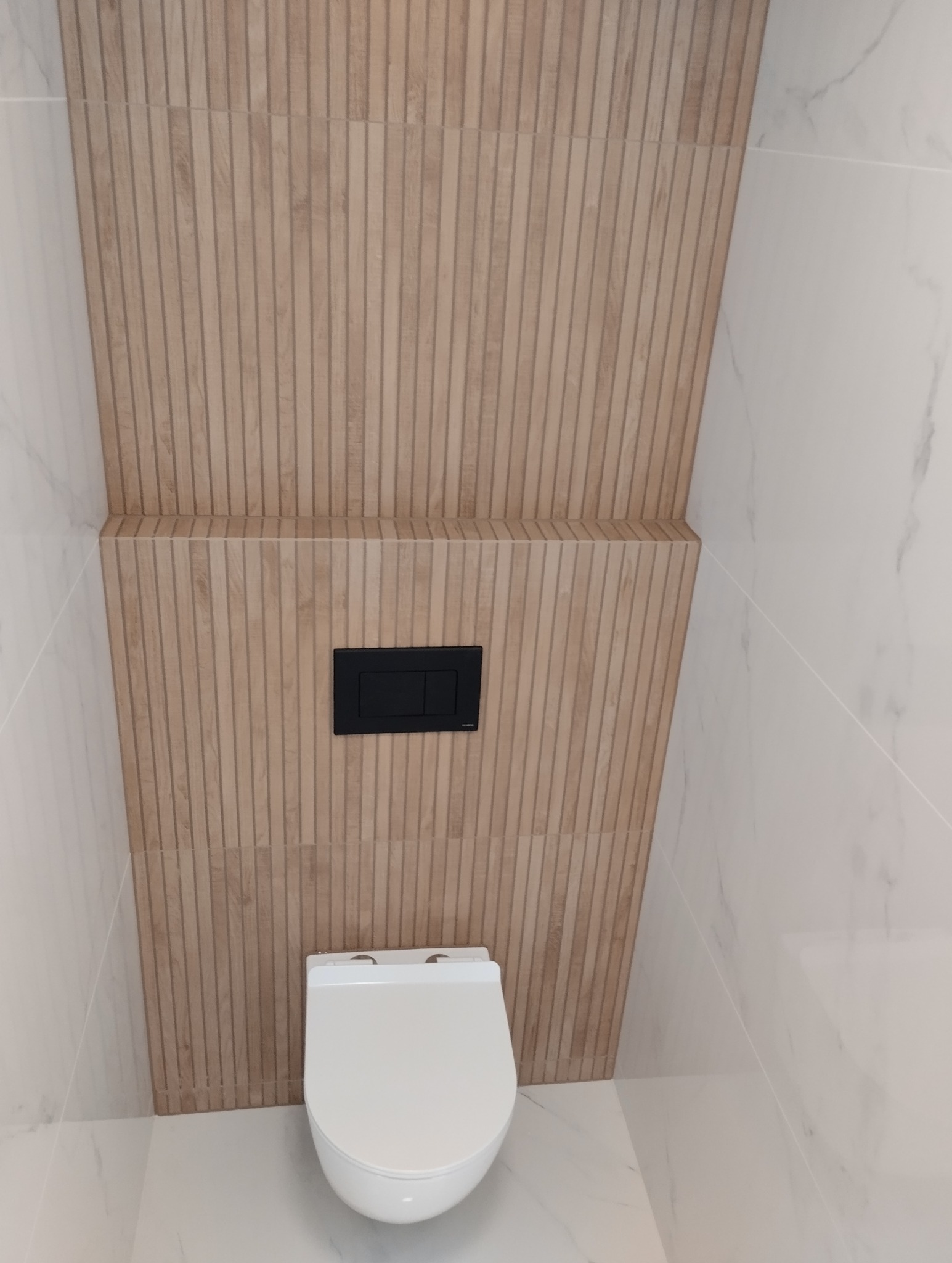 Nowoczesna łazienka: beżowe, ryflowane płytki imitujące drewno na ścianie za podwieszaną toaletą, kontrastująca z białymi marmurowymi płytkami po bokach.