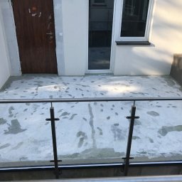 Oleg Bodnaruk BodChem - Biała posadzka na balkonie w trakcie prac, widoczne ślady stóp i niedociągnięcia, balustrada ze stali nierdzewnej z elementami szkła, drzwi wejściowe i okno w tle.