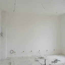 Wnętrze w trakcie prac wykończeniowych w Piekary Śląskie: świeżo pomalowane ściany na biało, widoczne wystające przewody elektryczne i puszki, na podłodze resztki materiałów budowlanych i narzędzia.