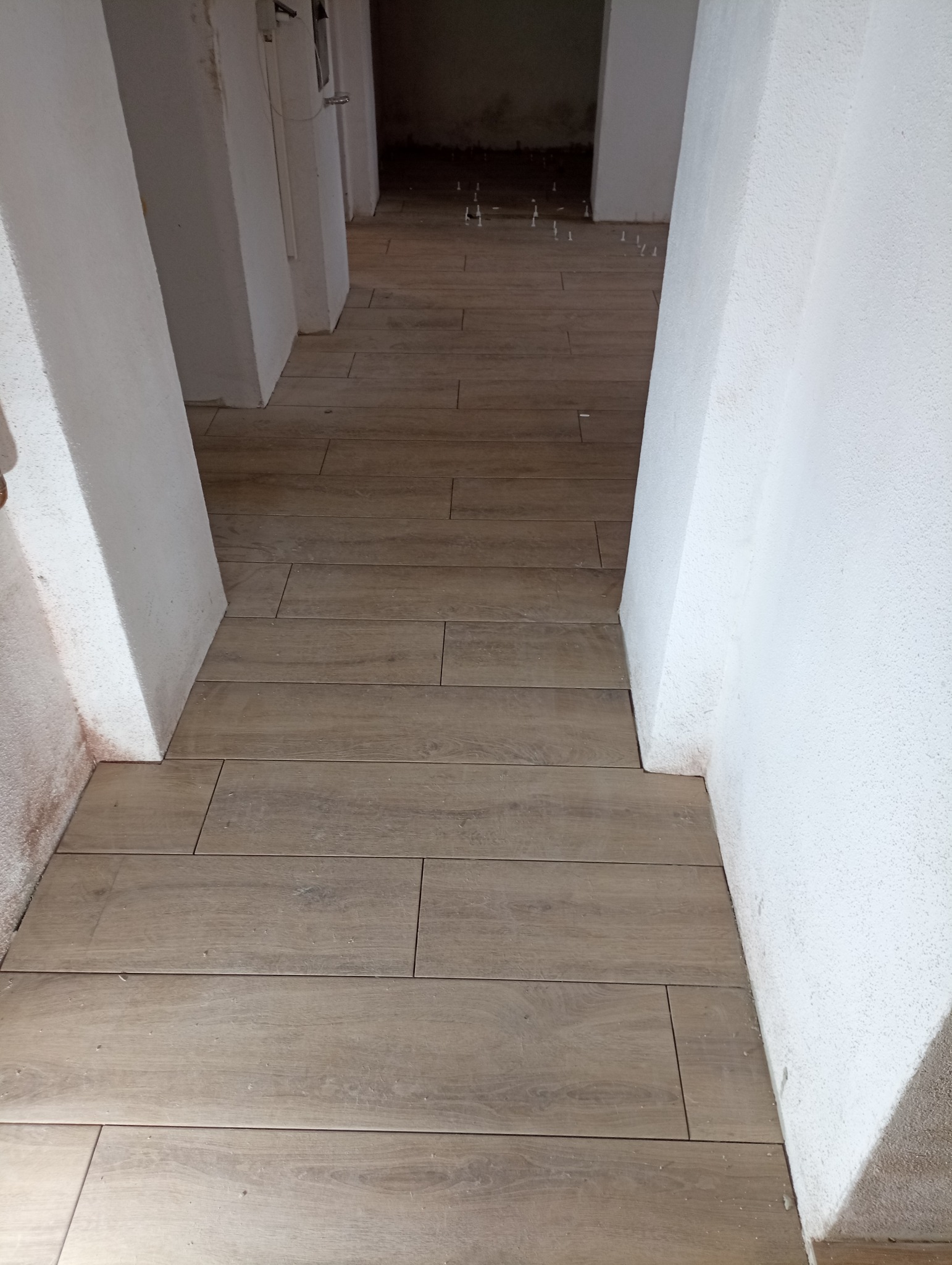 Ułożona podłoga z płytek imitujących drewno w korytarzu, widoczne krzyżyki dystansowe, ściany pomalowane na biało, surowy stan wykończenia.