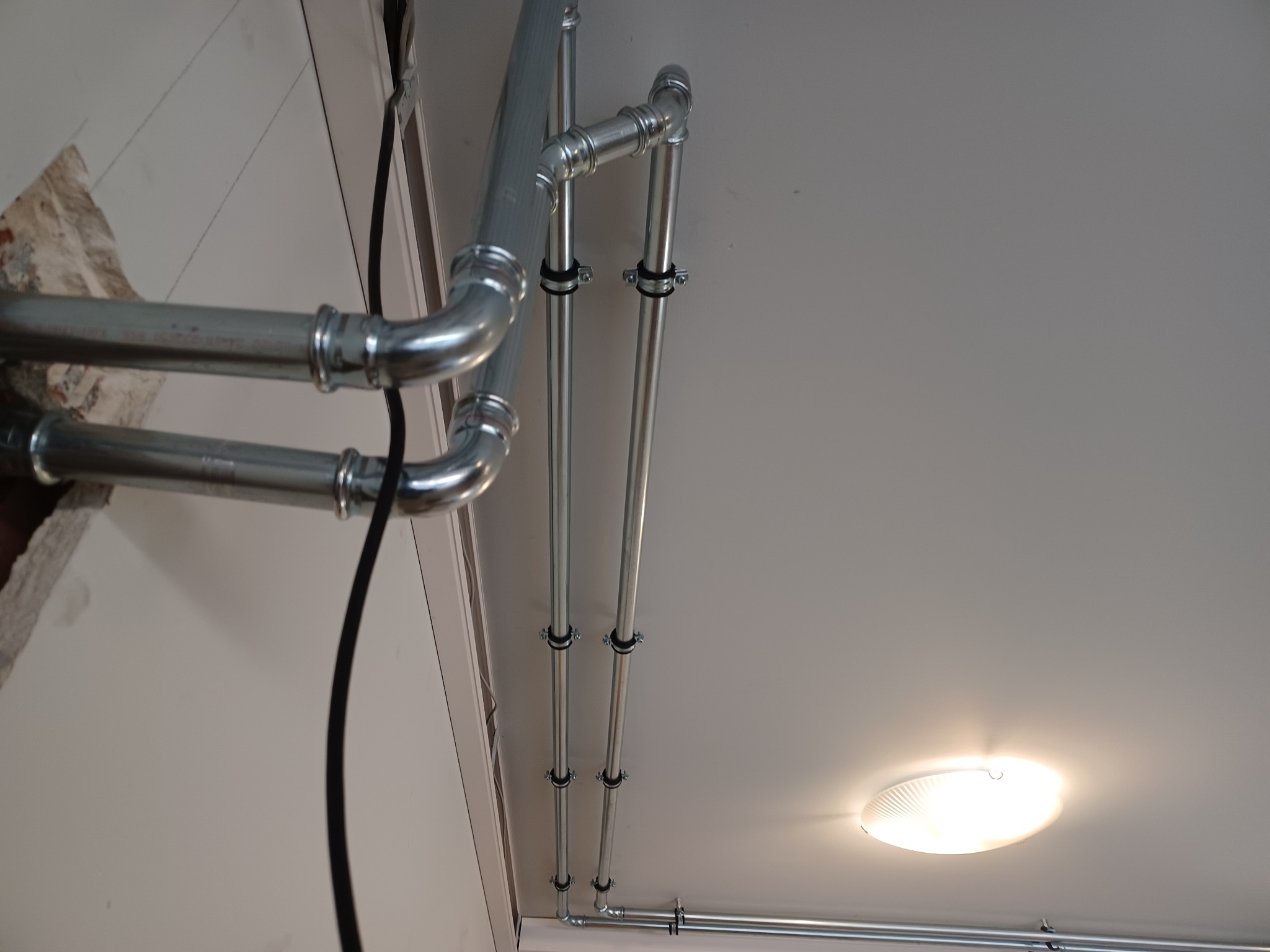 Metalowe rury instalacji gazowej zamontowane pod sufitem w Lipowej Górze Wschodniej, widoczne elementy mocujące i oświetlenie sufitowe.