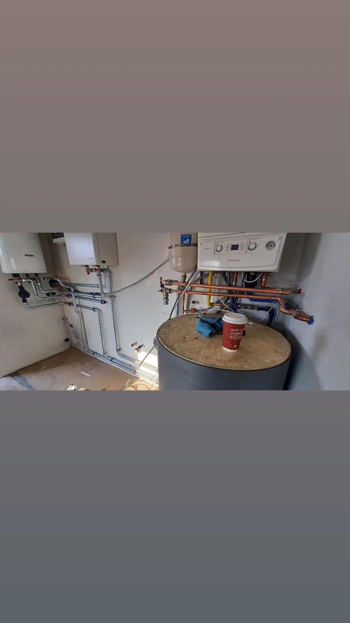 Nowa instalacja grzewcza z kotłem gazowym, zbiornikiem akumulacyjnym i rurami miedzianymi, widoczny kubek z kawą na zbiorniku.