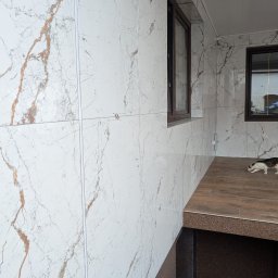 F.H.U. DS Elektryka & Glazura Dariusz Słembarski - Wykończona weranda z marmurowymi płytkami na ścianach i podłodze imitującej drewno. Widoczne okna z brązowymi ramami i kot na podłodze.