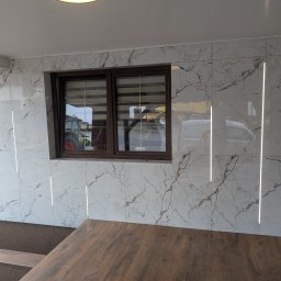 F.H.U. DS Elektryka & Glazura Dariusz Słembarski - Wykończony taras z marmurowymi płytkami ściennymi z oświetleniem LED, brązowymi ramami okiennymi i drewnianą podłogą. Widok na zewnątrz przez okno.