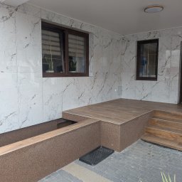 F.H.U. DS Elektryka & Glazura Dariusz Słembarski - Wykończony taras z marmurowymi płytkami ściennymi i brązowymi płytkami podłogowymi, z brązowymi oknami i drzwiami. Kot wchodzi do domu.