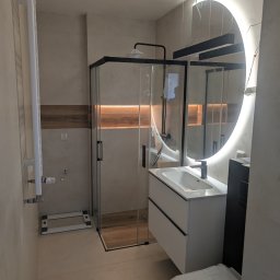 F.H.U. DS Elektryka & Glazura Dariusz Słembarski - Nowoczesna łazienka po remoncie: kabina prysznicowa z czarnymi ramami, umywalka z szafką, okrągłe lustro z podświetleniem LED i grzejnik.