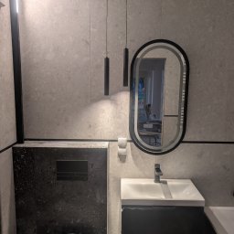 F.H.U. DS Elektryka & Glazura Dariusz Słembarski - Nowoczesna łazienka z szarymi płytkami, podwieszaną toaletą w czarnym dekorze i owalnym lustrem z podświetleniem. Minimalistyczne lampy wiszące.