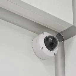 Kopułkowa kamera Bosch zamontowana w rogu pomieszczenia, widoczna srebrna listwa sufitowa i kolumna, białe ściany.