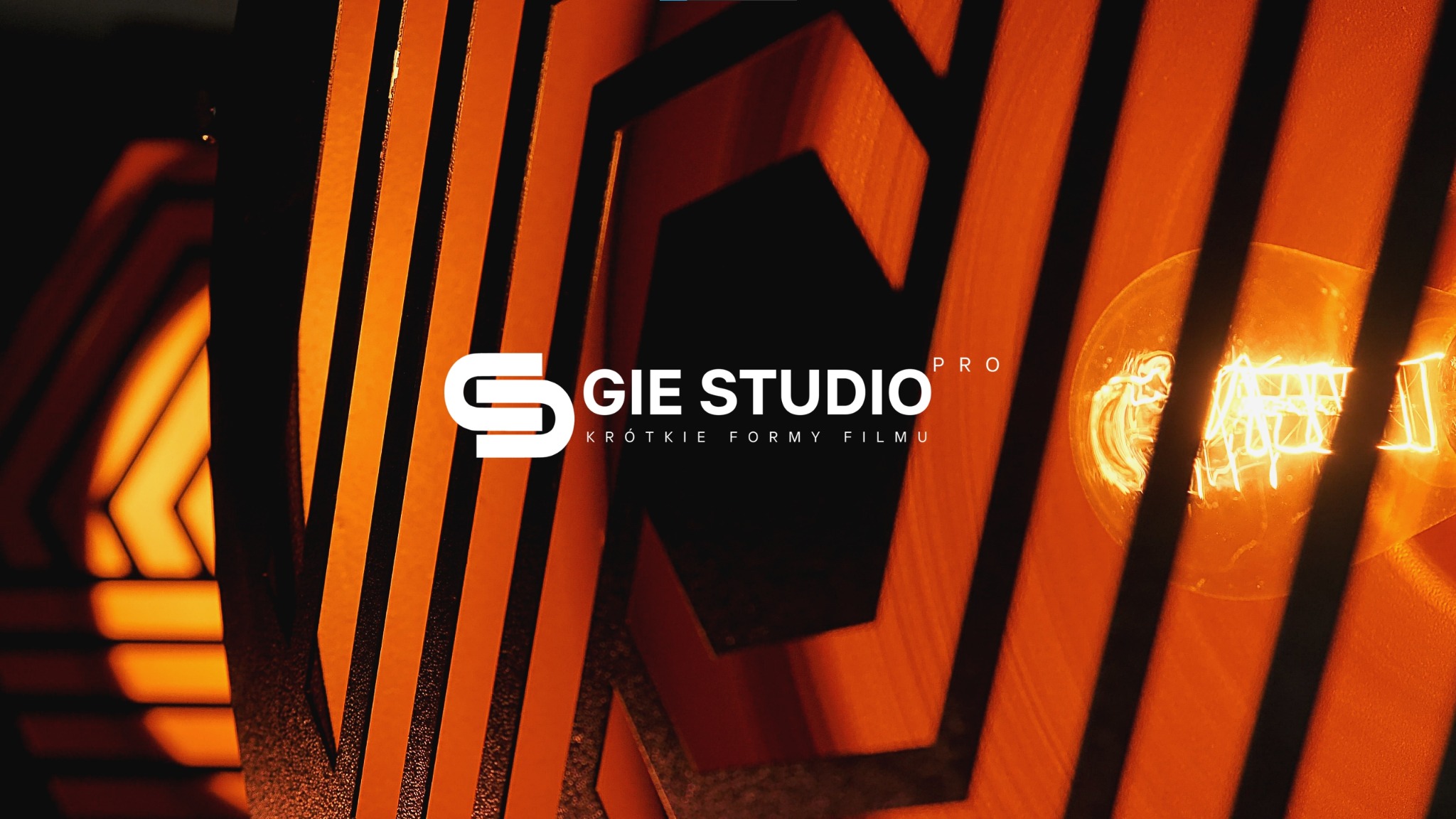Logo firmy GIE STUDIO PRO, specjalizującej się w krótkich formach filmu, z żarówką w tle i geometrycznymi wzorami w kolorze pomarańczowym.