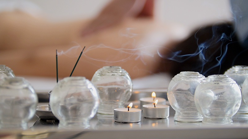 Szklane bańki do terapii, zapalone świeczki i kadzidła tworzą relaksującą atmosferę podczas zabiegu na plecach pacjenta.