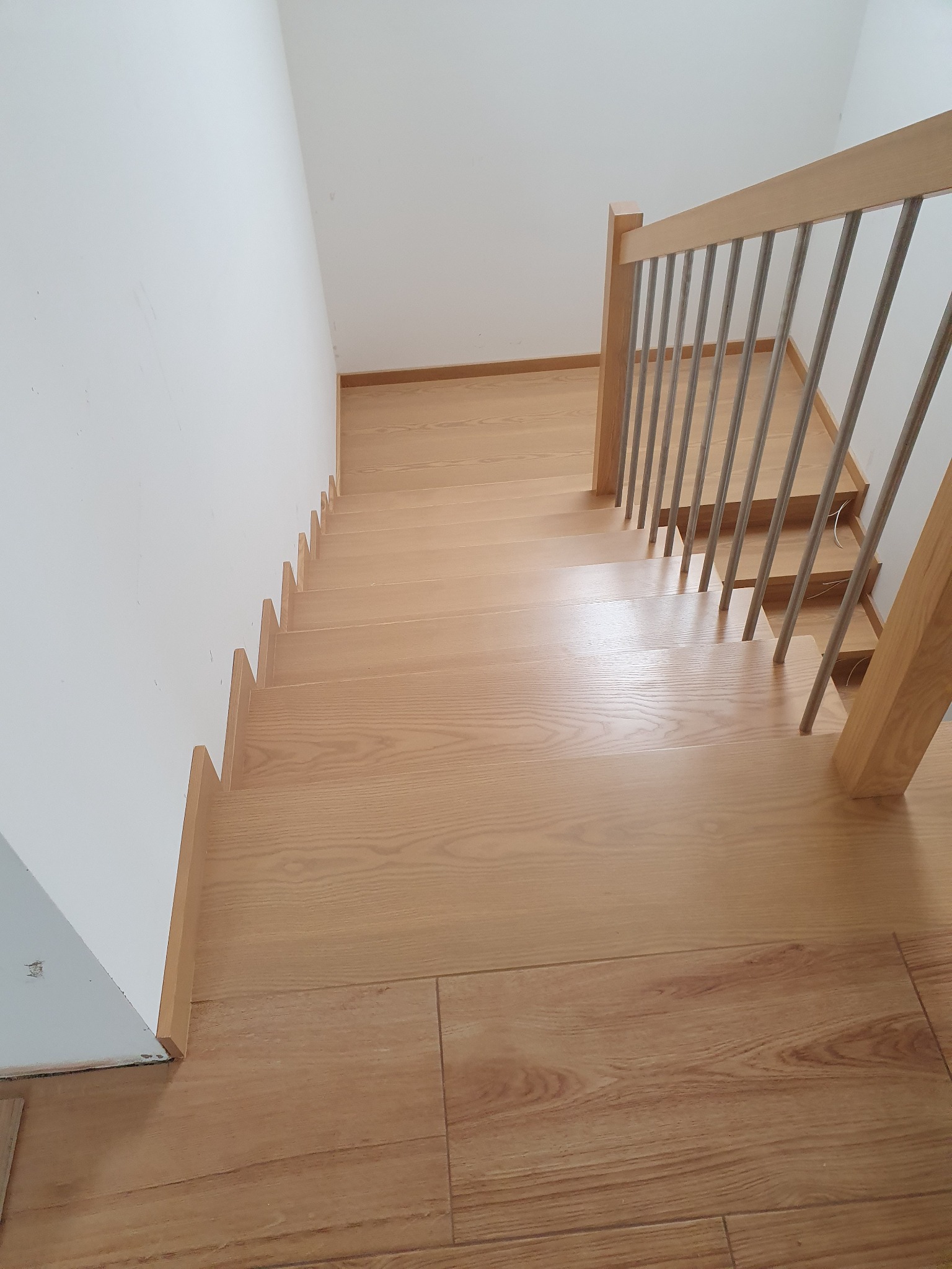 Jasne, dębowe stopnie schodów z metalową balustradą, widok z góry na dół, minimalistyczne wykończenie wnętrza.