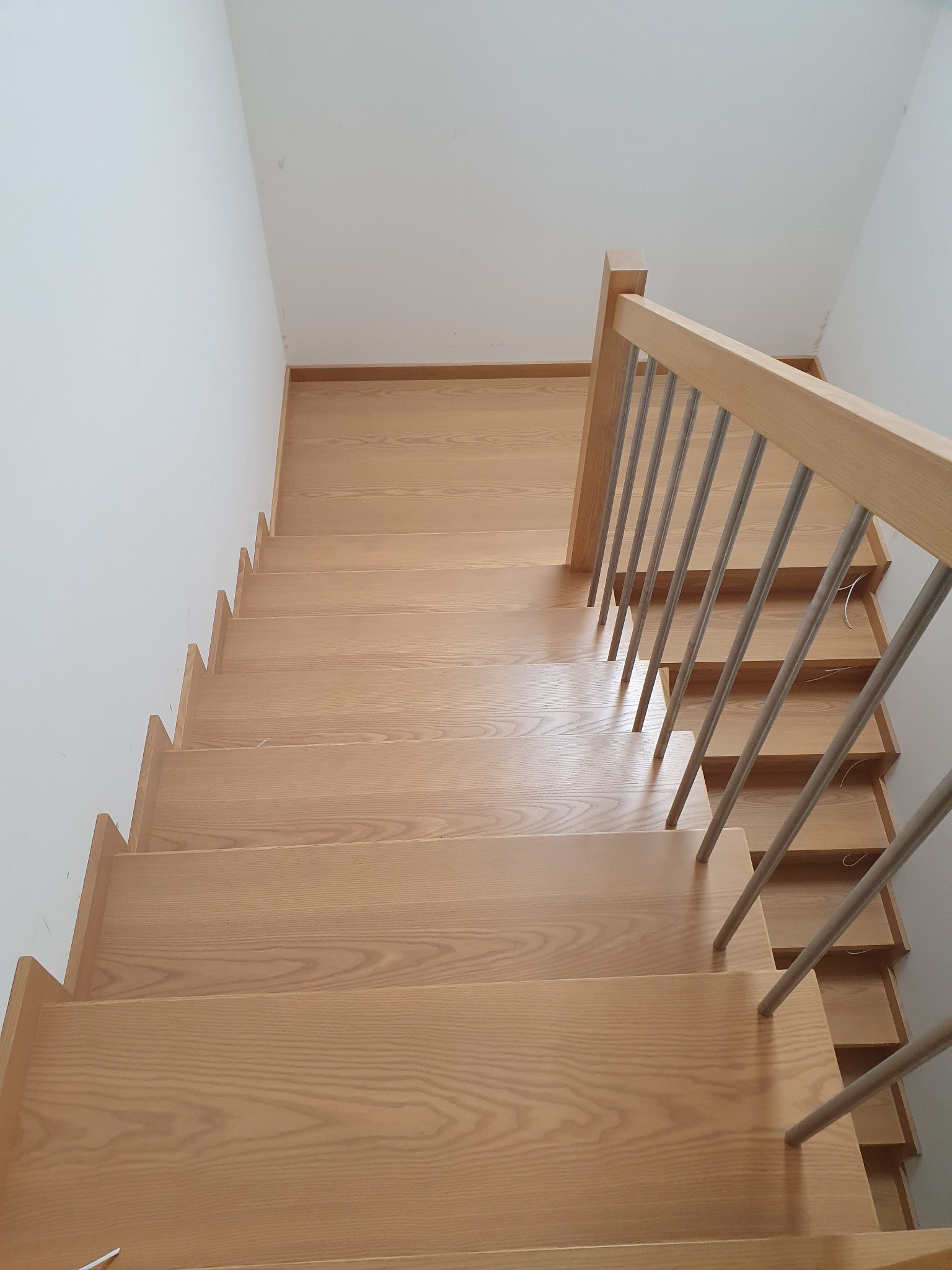 Jasne drewniane schody z metalowymi poręczami, widok z góry, minimalistyczny design, białe ściany.