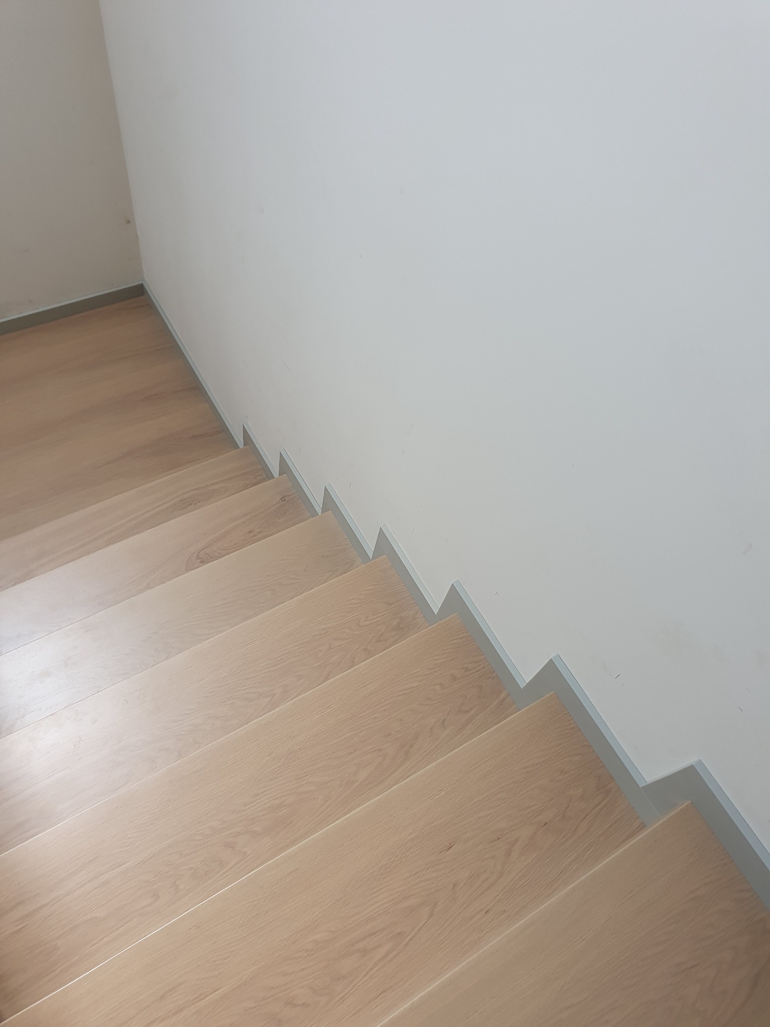 Jasne, drewniane stopnie schodów z szarą listwą przypodłogową, widok z góry, minimalistyczny styl.