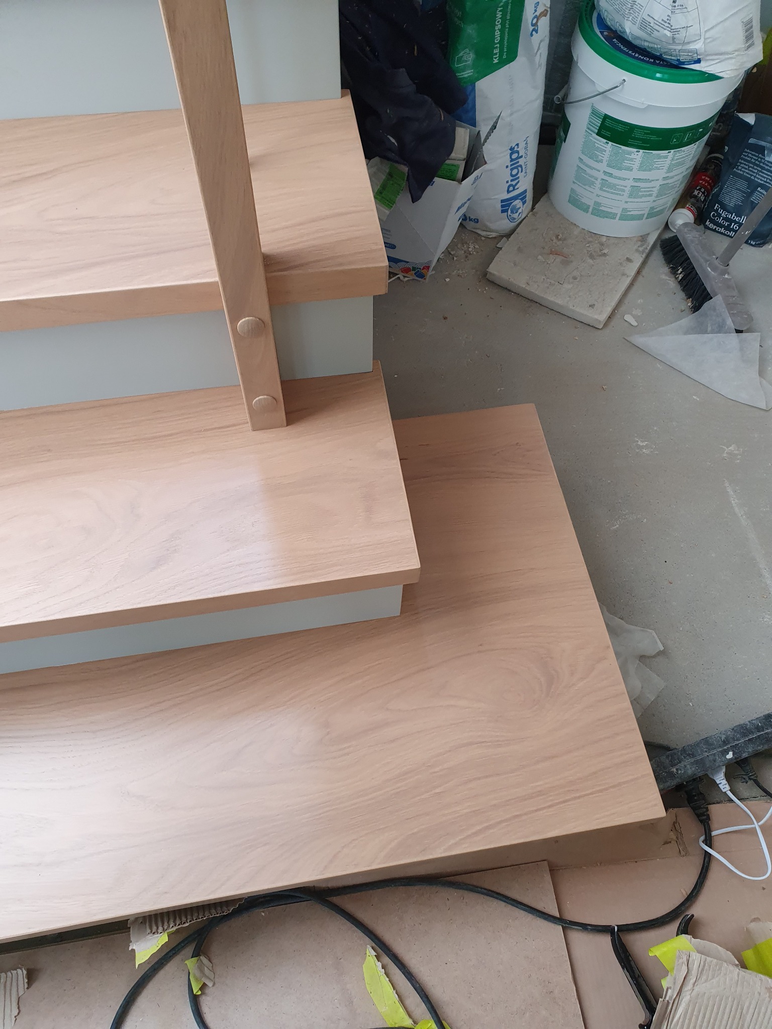 Fragment montowanych schodów z jasnego drewna z widocznymi elementami konstrukcyjnymi, na podłodze widoczne materiały budowlane i narzędzia.