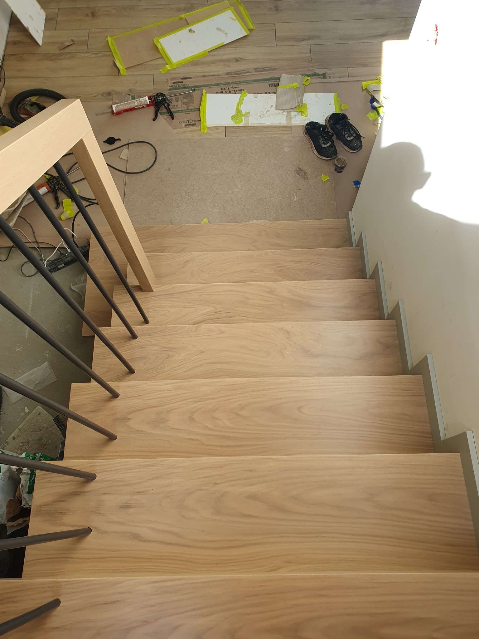 Montaż schodów: widok z góry na jasne, drewniane stopnie z metalową balustradą, w tle narzędzia i buty robocze na zabezpieczonej podłodze.