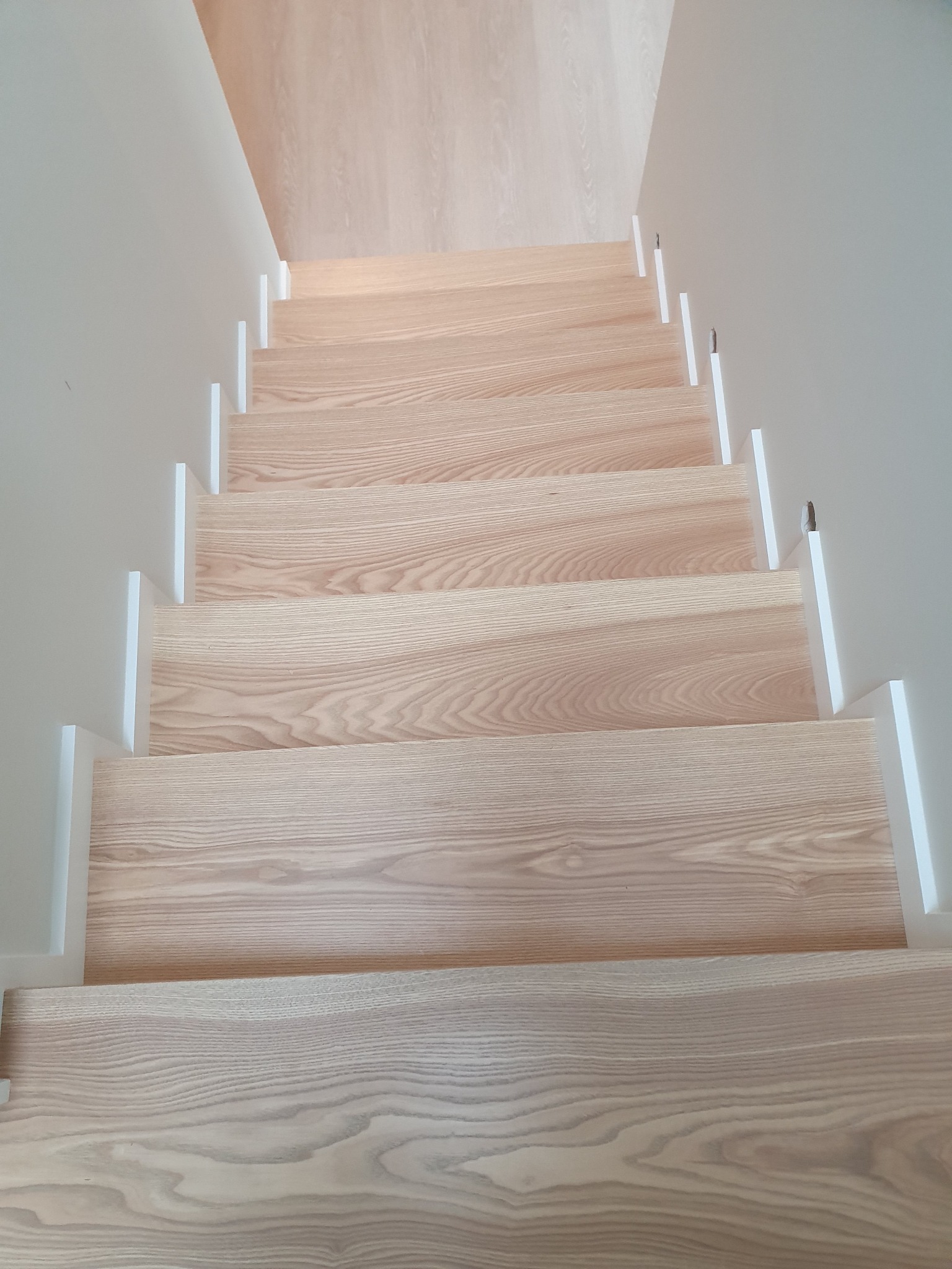 Jasne drewniane schody z białymi barierkami, widok z góry, naturalne usłojenie drewna.