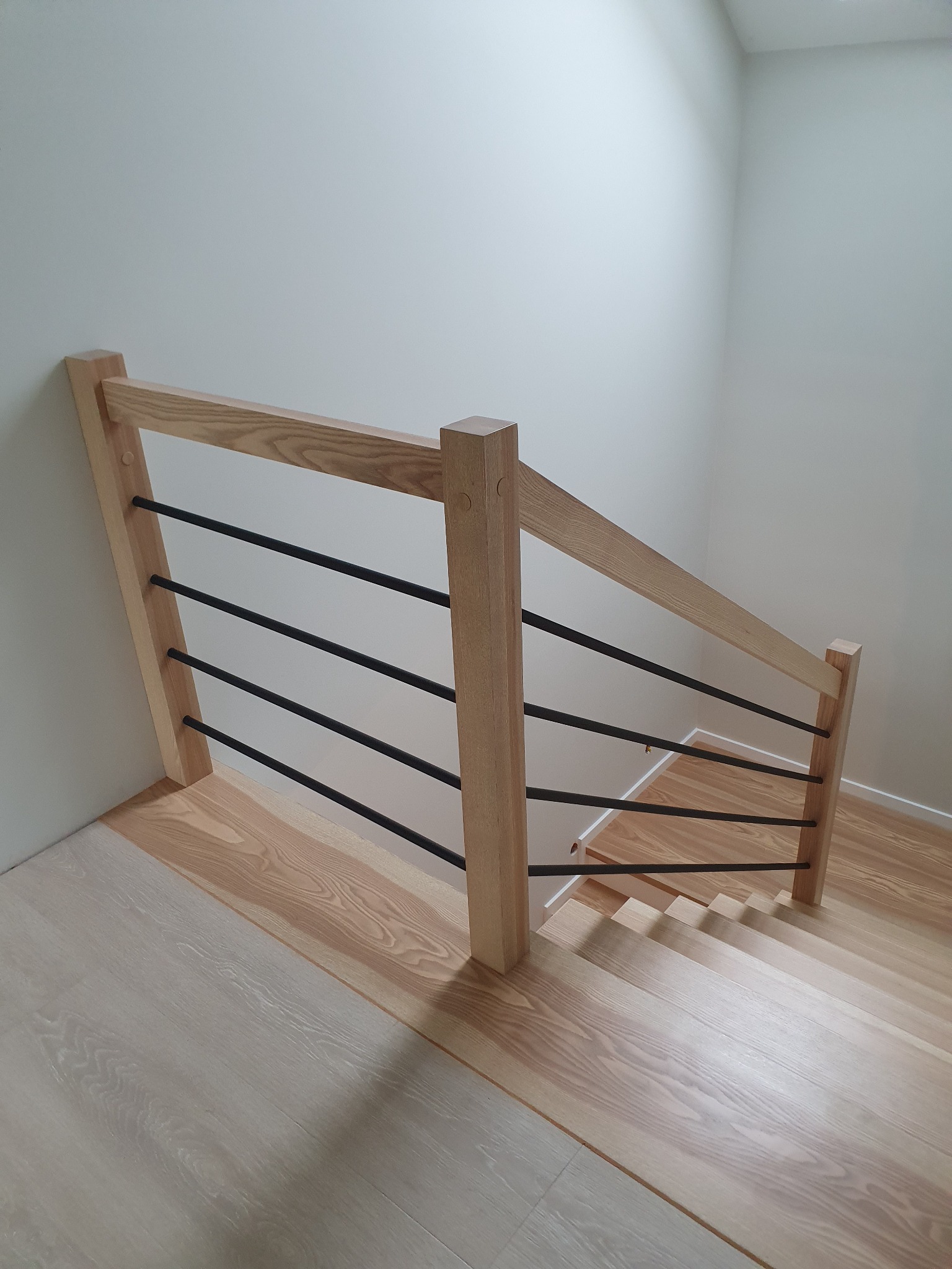 Nowoczesne schody z jasnego drewna z czarnymi, poziomymi balustradami, widok z góry.