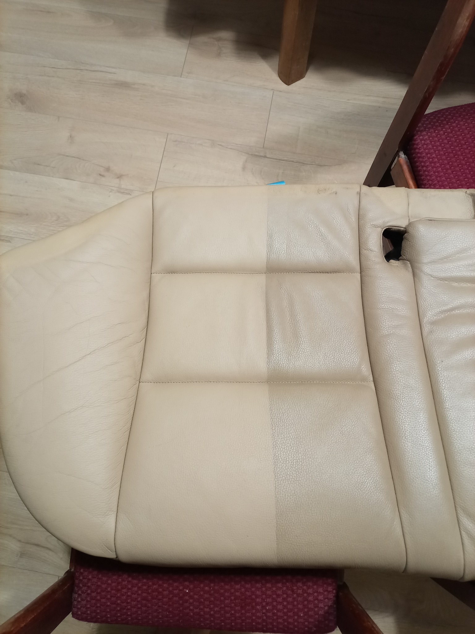 Fragment beżowego, skórzanego fotela samochodowego, z widoczną różnicą w czystości między lewą (przed) a prawą (po) stronie, umieszczonego na krześle z bordowym siedziskiem.