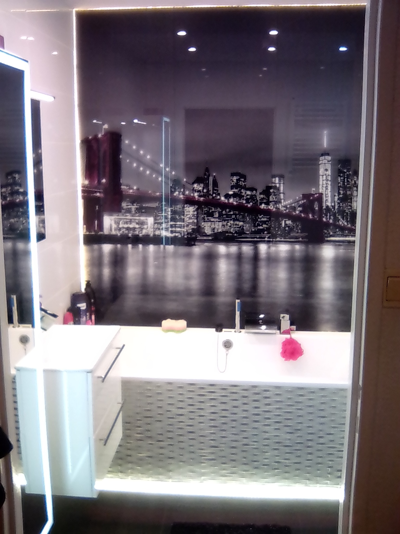 Nowoczesna łazienka w Olsztynie z podświetlanym blatem i fototapetą z panoramą miasta. Umywalka nablatowa i szara mozaika.