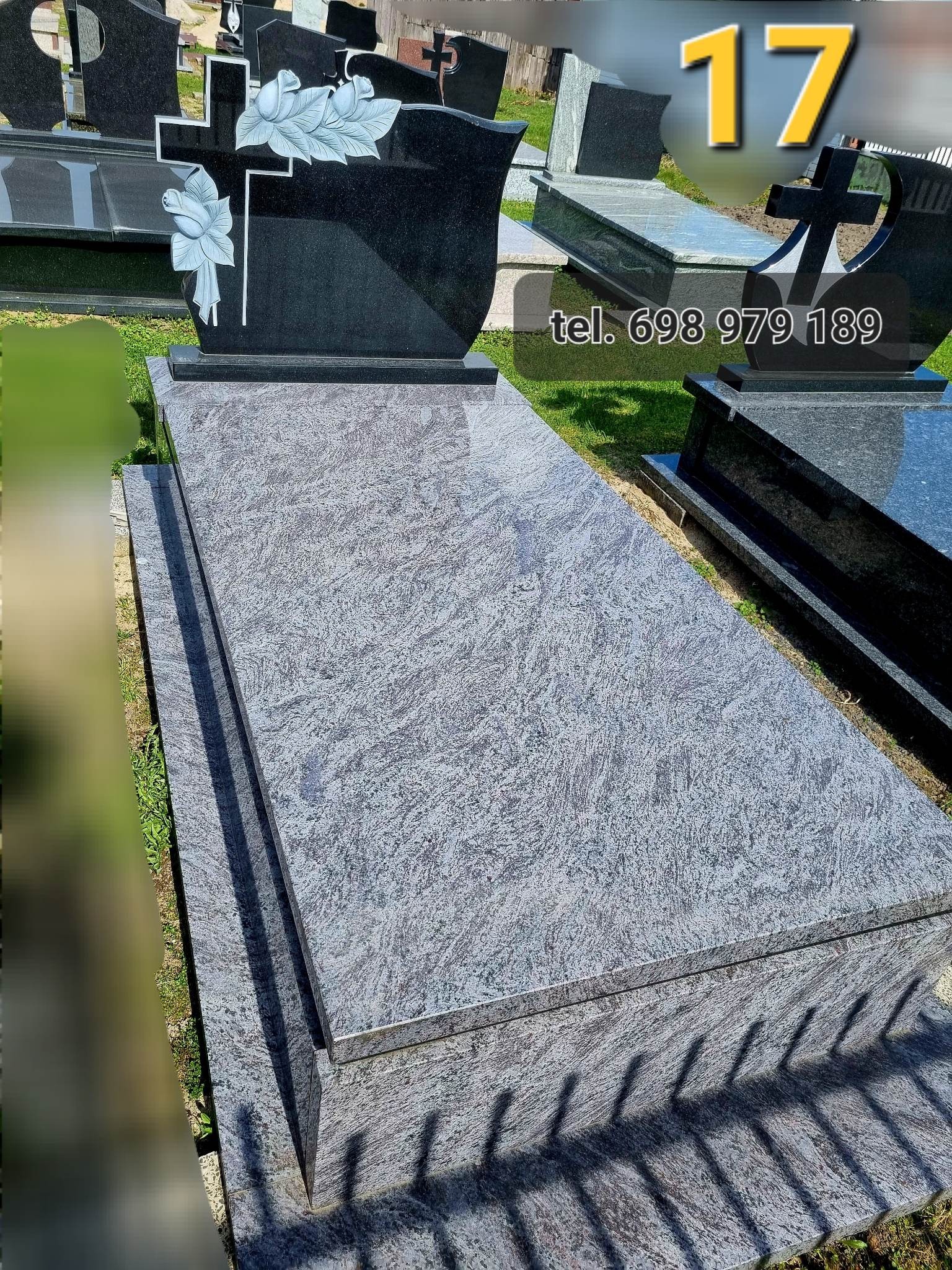 Granitowy nagrobek z krzyżem i motywem kwiatowym w Białej Podlaskiej, widoczny na tle innych nagrobków na cmentarzu.