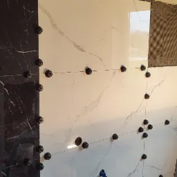 Ściana łazienki w trakcie układania płytek marmurowych w kolorze czarnym i białym, widoczne systemy poziomowania płytek i ślady kleju na ścianie, drabina oparta o ścianę