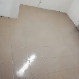 Beżowe płytki podłogowe ułożone w pomieszczeniu w trakcie remontu, widoczne ślady po zaprawie na ścianach, grzejnik w rogu.