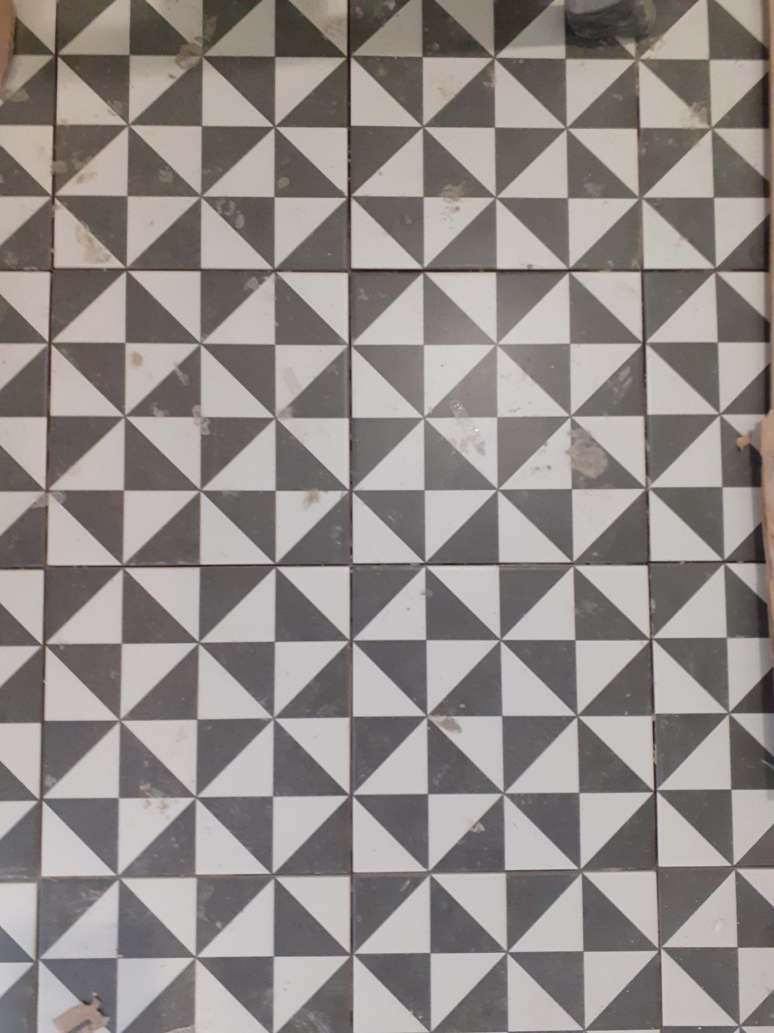 Ułożona podłoga z czarno-białych płytek w geometryczny wzór trójkątów, widoczne ślady po fugowaniu.