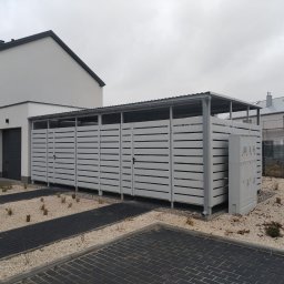 Markpol - Nowoczesny, szary garaż blaszany z poziomymi panelami, zadaszony, przylegający do domu z dwoma garażami, otoczony żwirem i kostką brukową.