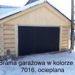 Markpol - Nowy garaż z jasnego drewna z czarną, ocieplaną bramą garażową w kolorze RAL 7016, pokryty śniegiem.