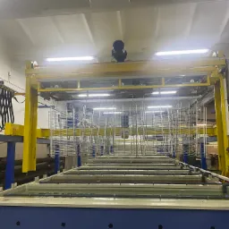 Linia do malowania proszkowego z zawieszonymi metalowymi elementami w koszach, przygotowana do zanurzenia w zbiornikach z roztworami.